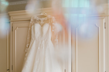 Modern bridal fashion. White wedding dress hanging in the hotel room.