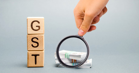 Wooden blocks with the word GST (Goods & Services Tax) and money. Tax, which is imposed on the sale...