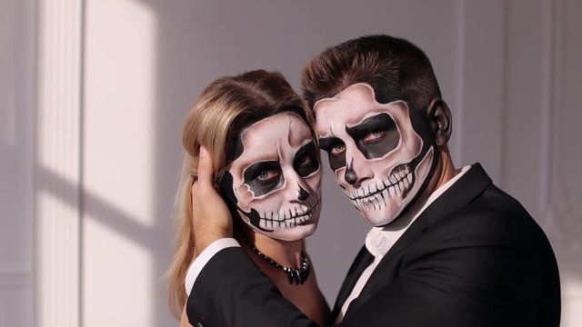 Portrait of a young couple in the Halloween mask. Close-up view of couple of painted halloween holy chracters woman and man. Loving young couple with sugar skull make-up.