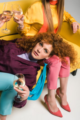 overhead view of attractive redhead woman lying on sofa and holding champagne glass near girls on white