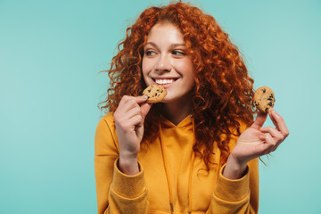 Portrait of alluring redhead woman 20s smiling and eating sweet cookies