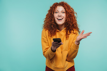 Portrait of excited redhead woman 20s smiling and using cell phone