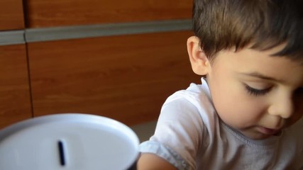 cute two years old saving money, putting coins in metal bank
