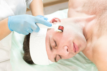Obraz na płótnie Canvas Young man on the procedure of rejuvenation and cleansing of the skin of the modern medical instrument derma roller. 