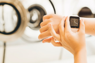 Close up woman hand with watch in modern laundry room. Concept of saving time.