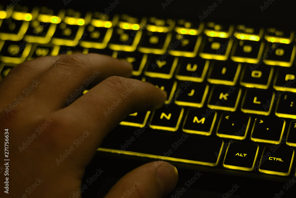 Poster man's hand typing on keyboard with yellow backlight