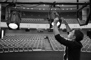 A young guy mounts lighting equipment on the stage of the theater