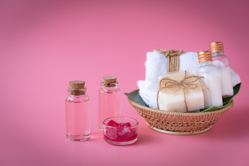 Spa wellness concept with red candle,rose liquid bottle,milk soap,white towels in wooden tray on pink background
