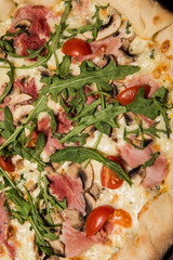 top view closeup of pizza with arugula, ham, mushrooms and tomatoes
