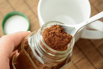 White cup, jar of coffee and a green cover lays on brown background. Taking some coffee from a jar...