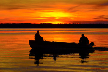 silhouettes of fishermen on a boat at sunset, floating by the shore