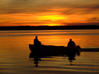 silhouettes of fishermen on a boat at sunset, floating by the shore