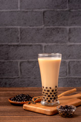 Delicious bubble milk tea with tapioca pearl ball in glass on wooden table and dark gray brick background, popular food and drink in Taiwan, close up