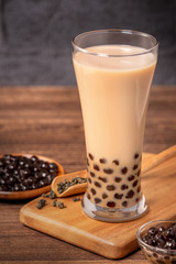 Delicious bubble milk tea with tapioca pearl ball in glass on wooden table and dark gray brick background, popular food and drink in Taiwan, close up