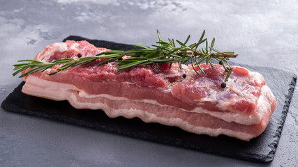 Raw pork brisket with salt, pepper and rosemary on a black stone.