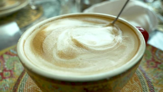 Woman sitting at the table, drinking coffee with cinnamon buns, stiring coffee closeup