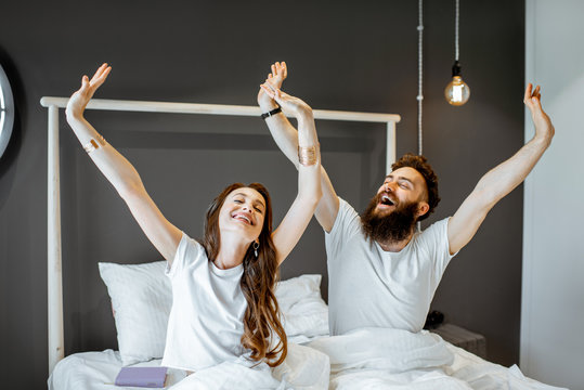 Happy couple waking up with raised hands, feeling good in the morning at home