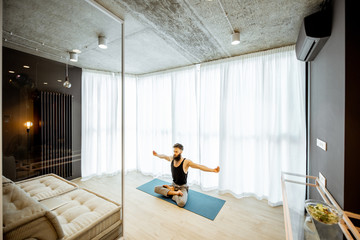 Wide view on the living room of the modern apartment with man practising yoga indoors