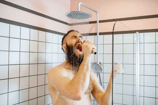 Joyful bearded man singing into the micrphone while taking a shower in the bathroom