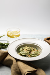 green ravioli with pine nuts and sage at wooden table with napkin and water with lemon isolated on grey