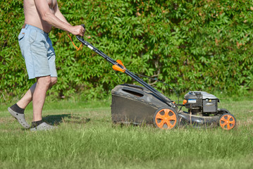 Man is using lawn mower on his countryside yard.