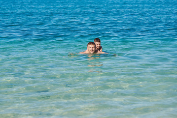 European man and his son are swimming in the ocean together during their vacations. Healthy lifestyle.