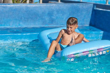 Caucasian boy having fun in swimming pool at resort. He is using inflatable mattress.