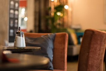 A sugar shaker sits on the table of a modern coffee shop.