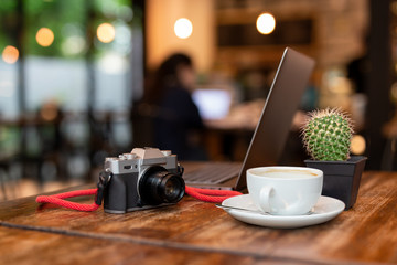 Cup of coffee and camera with  laptop on wooden table.