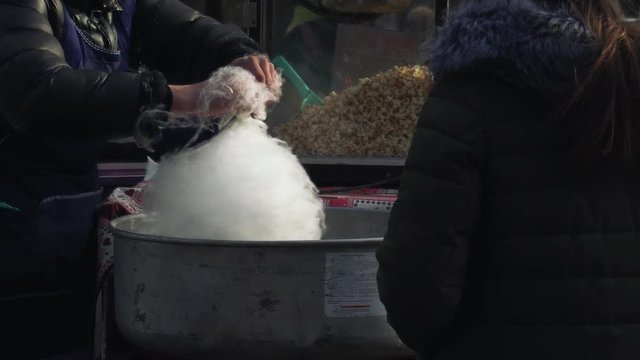 A person spins white cotton candy with an automated machine at a funfair. A seller makes white candy floss with a modern machine at the amusement park.