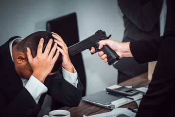 A businesswoman carrying a gun at the head of a young businessman because of a betrayal in the trading of stocks and investments. Intimidation and cheating concept. - obrazy, fototapety, plakaty