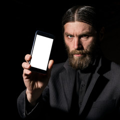 Old believer senior priest with a smartphone, bearded old man is calling on a dark background
