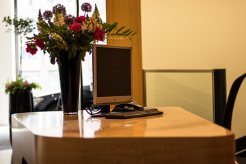 A modern reception area featuring a PC with a blank screen and a vase of flowers.