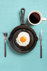 black frying pan with scrambled eggs, fork, knife, with cup of coffee on a turquoise tablecloth