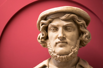A white statue of a male in front of a red background.