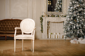 Classic Christmas decorated interior room New year tree. Christmas tree with gold decorations. Modern white classical style interior design apartment with fireplace and armchair.