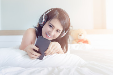 young asian girl in the white bedroom is relaxing by listening to her favourite music via the internet online on weekend