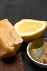 close up view of aromatic oil in bowl with spices and herbs near lemon and cheese