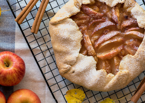 Rustic apple open galette pie with sweet filling on a light background. Flat pie with apples and autumn leaves on a white tablecloth. Top view, flat lay.