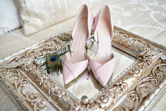 Beautiful pink bride shoes on high heels and peacock feather on vintage mirror on bed, copy space. Luxury bridal accessories. Wedding morning preparations