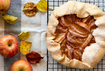 Rustic apple open galette pie with sweet filling on a light background. Flat pie with apples and autumn leaves on a white tablecloth. Top view, flat lay.