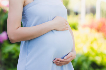 A pregnant woman in a blue dress on a nature background close-up. Pregnancy, parenthood, motherhood concept. Love for children concept with copy space.