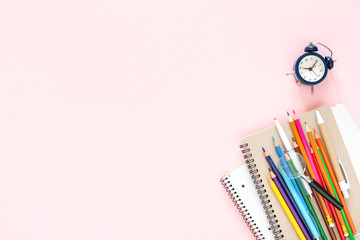 School stationary on pink background. Notebooks, pens, color pencils and alarm clock. Back to School concept.