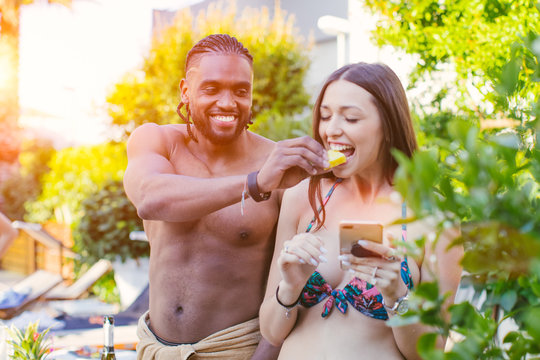 African American guy giving a piece of pineapple (feeding) to his white girlfriend - natural authentic image of multiracial couple taking care of each other - love and healthy food concept