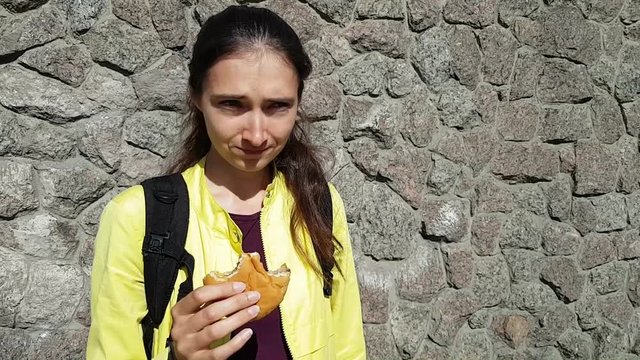 The girl has the hiccups while eating. Funny emotions. A quick snack with a hamburger bun on the street. Dried meat