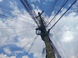 Jumbled up cables on a concrete pole with  blue sky on the background