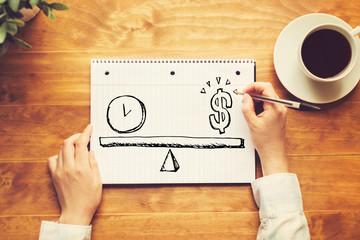 Time and money on the scale with a person holding a pen on a wooden desk