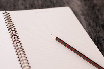 Notepad with pencil on wooden table background.