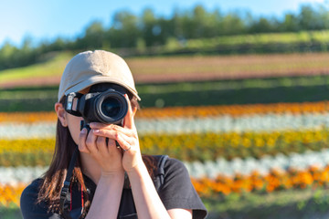 Close-up a Young Japanese girl holding a digital camera and taking photo in a colorful flowers field in summer sunny day at Shikisai-no-oka, popular spot for sightseeing in Biei Town, Hokkaido, Japan