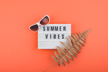 Summer vacations trip flat lay with Summer vibes text on light box, golden tropical leaves and...